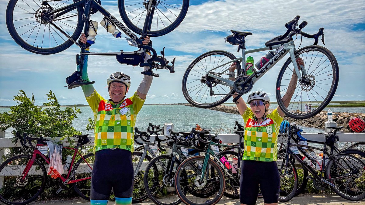Jack and Kayla holding their bikes overhead at the Pan-Mass Challenge finish in Provincetown